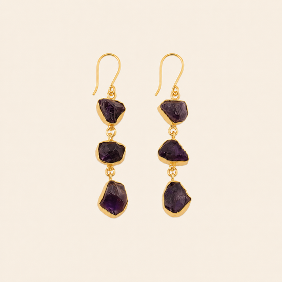 Gold earrings with purple gemstones on a beige background