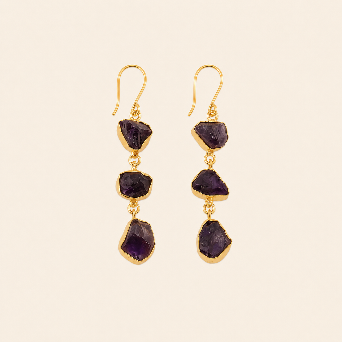 Gold earrings with purple gemstones on a beige background