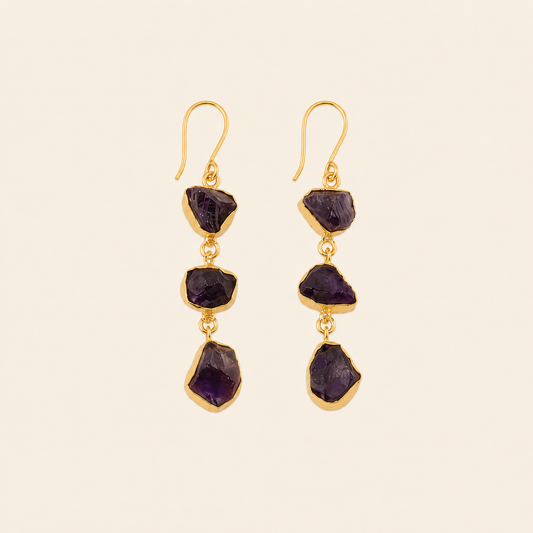 Gold earrings with purple gemstones on a beige background