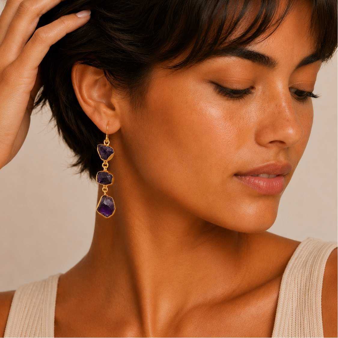 Close-up of a woman wearing gold and purple dangling earrings against a neutral background