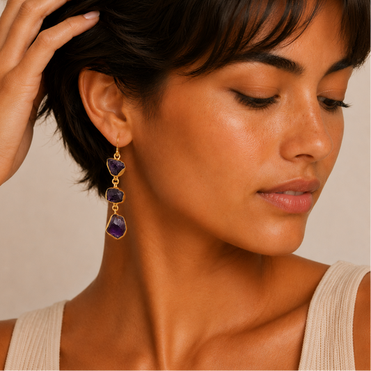 Close-up of a woman wearing gold and purple dangling earrings against a neutral background