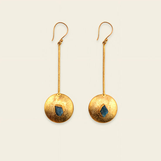Gold earrings with circular designs and blue stones on a beige background