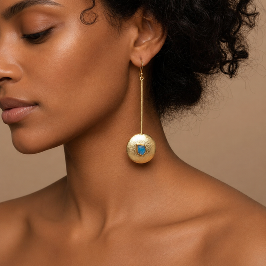 Close-up of a woman wearing a gold earring with a blue gemstone on a beige background