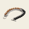 A beaded chain bracelet featuring natural brown wood beads, matte black beads, a silver braided chain, and a textured silver clasp on a light beige background.