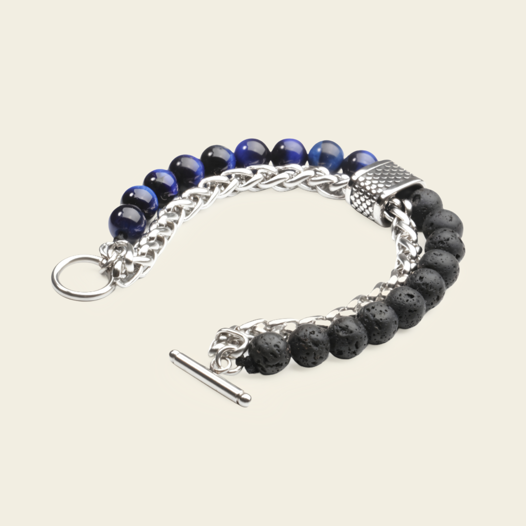 A beaded chain bracelet featuring dark blue and black beads, silver-tone chain links, a textured metal clasp, a ring, and a toggle clasp, shown on a light beige background.