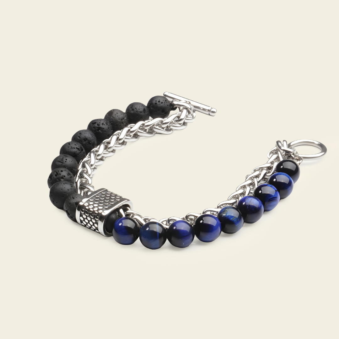 A men's beaded bracelet featuring black lava stone beads, polished dark blue lapis lazuli beads, a silver-tone chain link section, and a textured silver clasp on a light beige background.