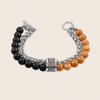 A men's beaded and chain bracelet featuring matte black beads on one side, polished orange-brown wooden beads on the other, and a textured silver-toned center clasp, shown on a light beige background.
