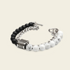 A silver chain bracelet featuring matte black round beads, white marble round beads, and a textured silver cube clasp, displayed on a light beige background.
