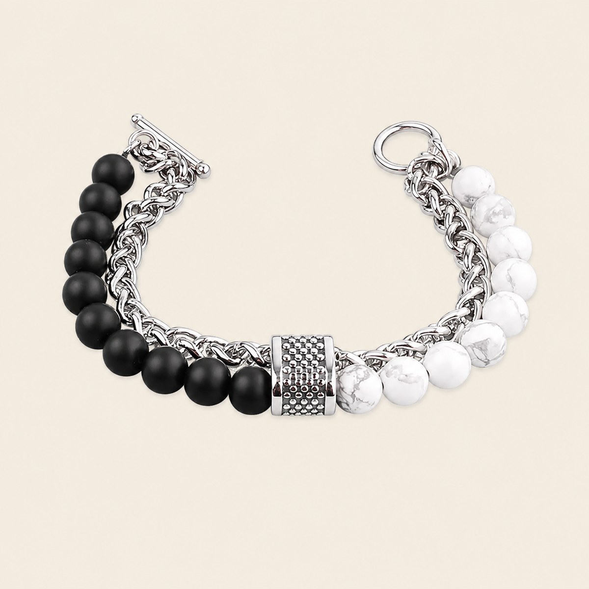 A silver-toned chain bracelet featuring one side with matte black beads and the other with white marbled beads, finished with a textured central cap and toggle clasp, shown on a light beige background.