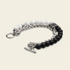 A men's multi-strand bracelet featuring silver-tone chain links, a textured silver spacer, white marbled beads, and matte black round beads, finished with a toggle clasp on a light beige background.