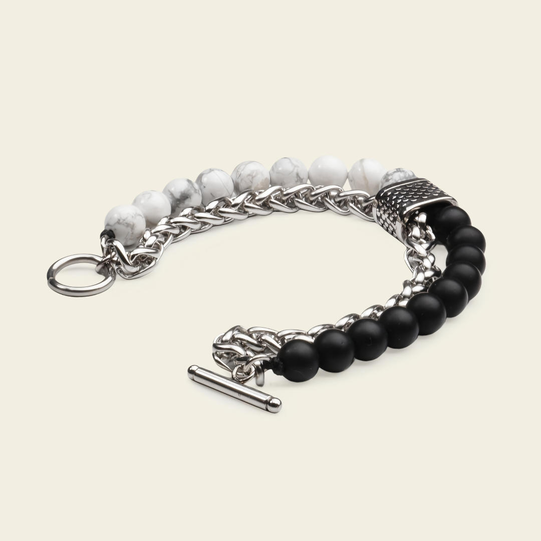 A men's multi-strand bracelet featuring silver-tone chain links, a textured silver spacer, white marbled beads, and matte black round beads, finished with a toggle clasp on a light beige background.
