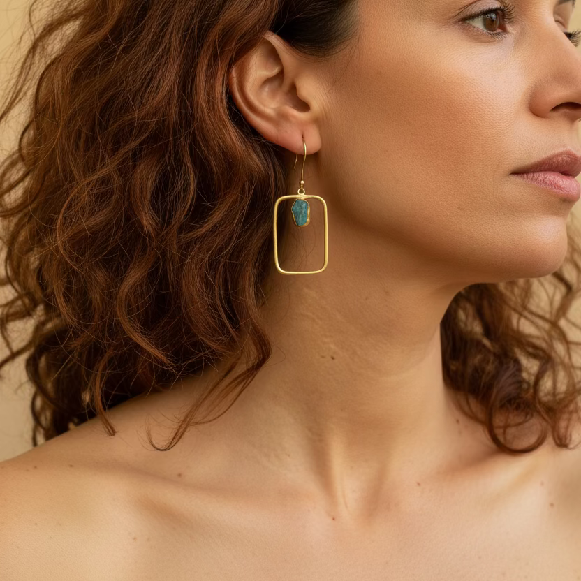 Close-up of a woman wearing gold earrings with a green gemstone.