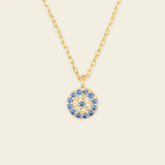Gold necklace with a blue and white gemstone pendant on a beige background