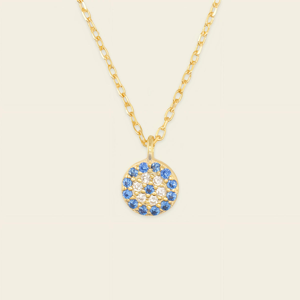 Gold necklace with a blue and white gemstone pendant on a beige background