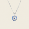A silver chain necklace with a circular pendant featuring a blue and white eye design, set against a solid light beige background.