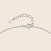 Close-up of a silver chain necklace showing a lobster clasp, extension chain, and a small engraved teardrop tag on a light beige background.