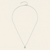 A delicate silver chain necklace with a small round bezel-set clear gemstone pendant, displayed on a light cream background.