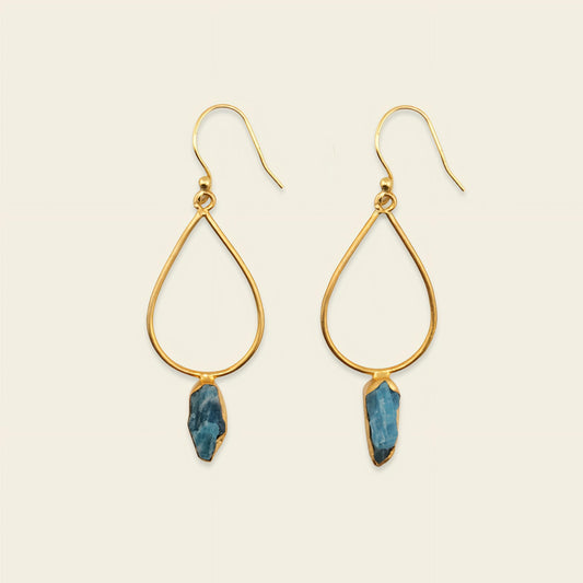A gold earring with a blue gemstone against a neutral background