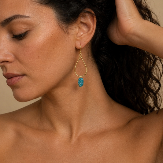 Close-up of a woman wearing a gold earring with a blue gemstone against a neutral background