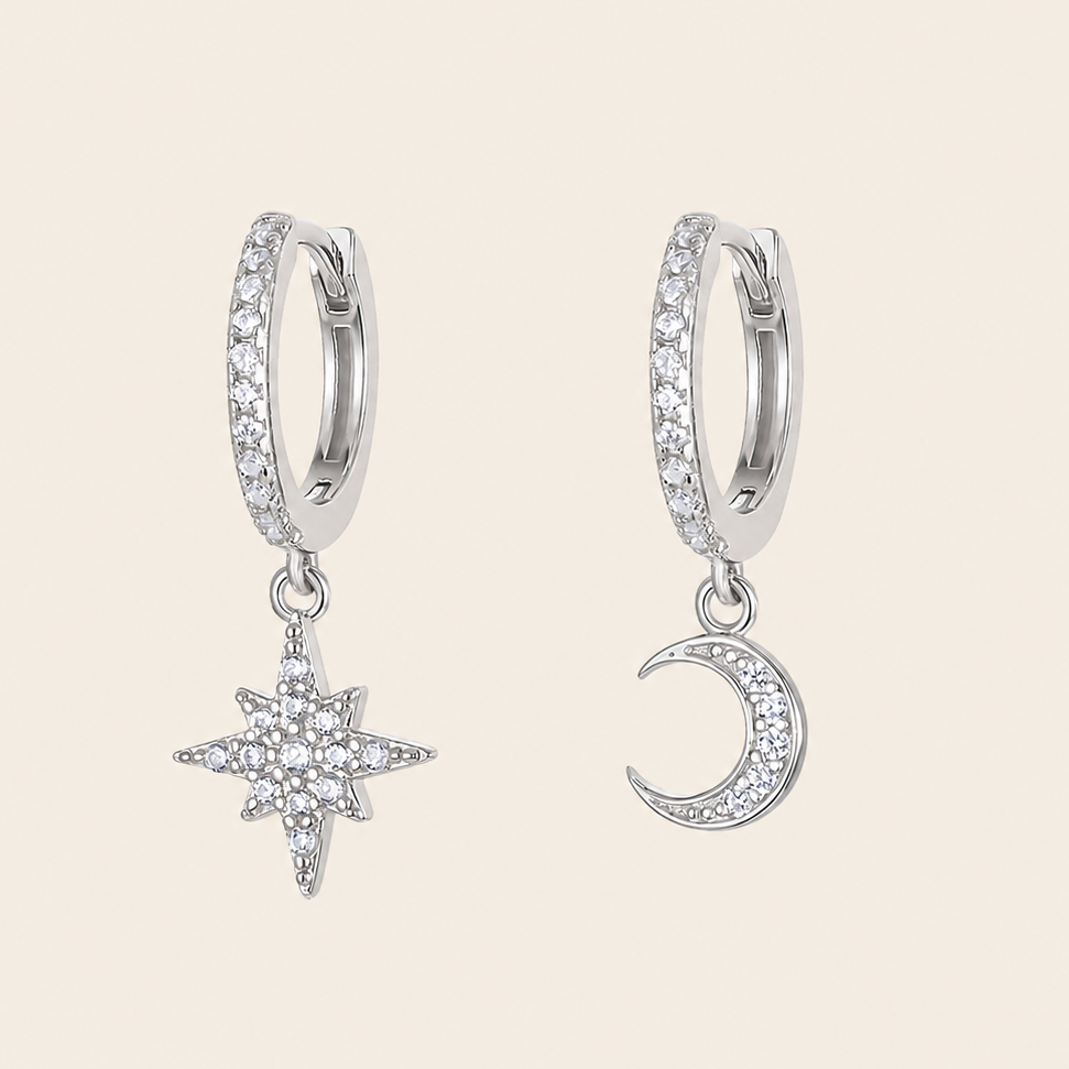 Silver hoop earrings with star and moon charms on a beige background