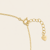 Close-up of a gold chain necklace extender with a heart-shaped pendant on a light cream background.