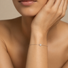Close-up of a woman's arm wearing a delicate bracelet with a small diamond on a neutral background