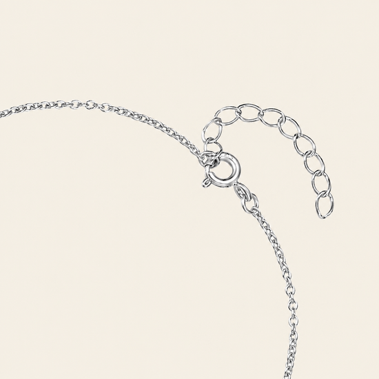 Close-up of a silver chain necklace with a lobster clasp and an adjustable oval link extender, shown on a light cream background.