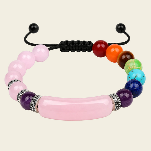 A beaded adjustable cord bracelet featuring a large central pink stone bar, pink beads, silver spacer details, and a rainbow sequence of colored beads on a light beige background.