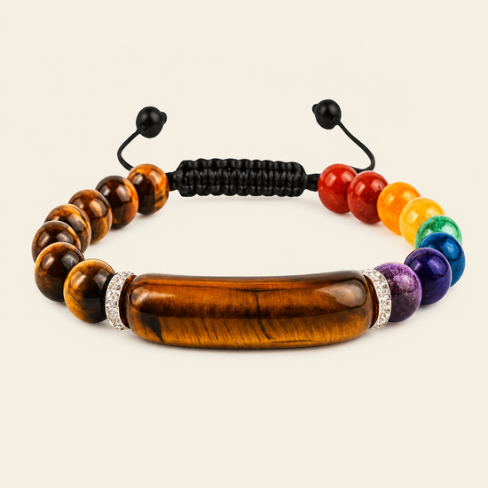 A beaded chakra bracelet featuring a large polished tiger's eye bead at the center, surrounded by rainbow-colored gemstone beads, silver rhinestone spacers, and a black adjustable cord closure, shown on a light beige background.