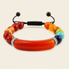 A beaded bracelet featuring a large, smooth, curved red-orange central bead, flanked by smaller red, orange, yellow, green, and blue beads, with a black adjustable cord and silver-tone spacer details, shown on a light beige background.