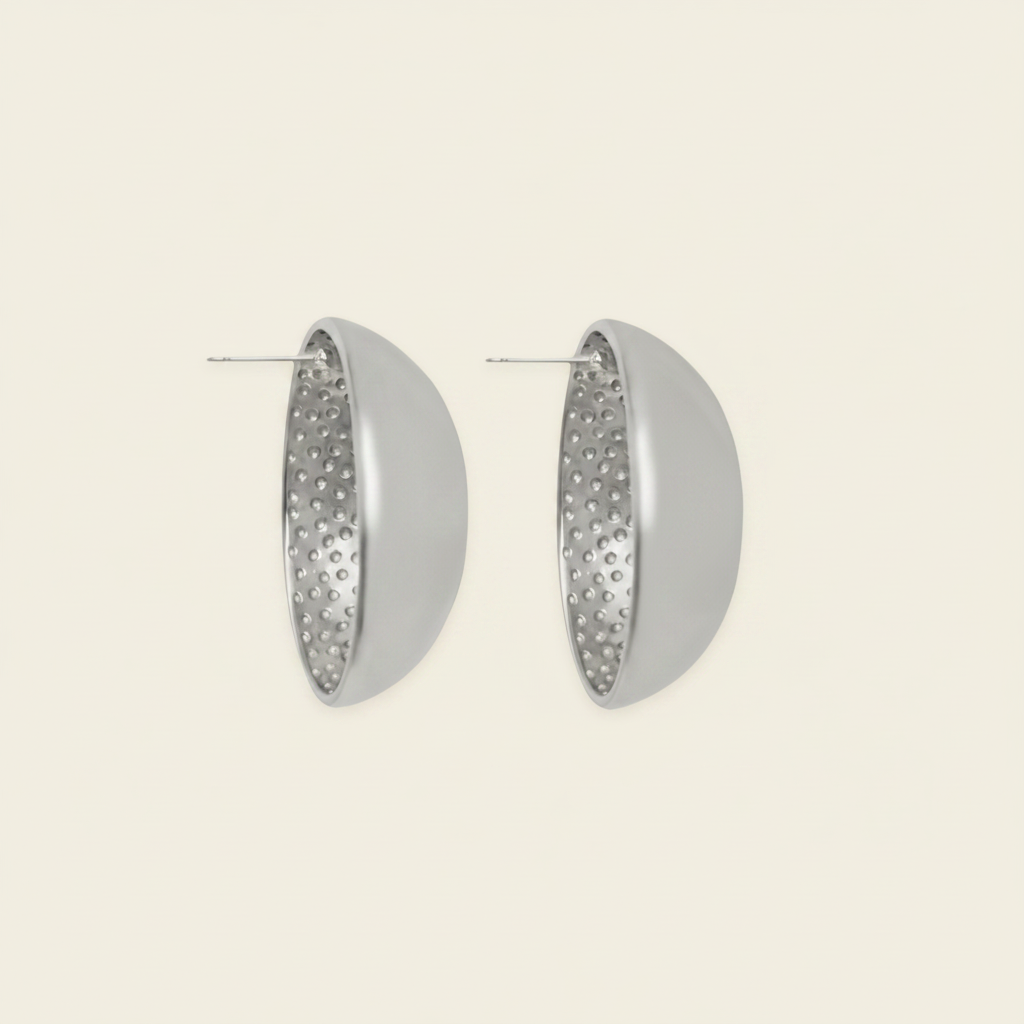 A pair of silver-toned geometric hoop earrings with a smooth outer half and a textured, dimpled inner half, shown on a light cream background.