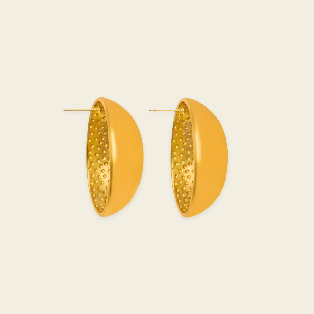 A pair of gold-toned geometric hoop earrings with a smooth outer half and a textured, dimpled inner half, shown on a light cream background.