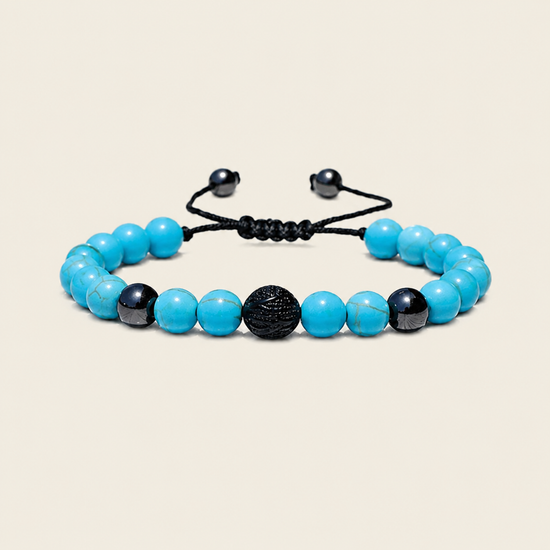 A beaded stretch bracelet featuring bright turquoise-blue beads, black marbled beads, and a central textured black sphere, strung on a black adjustable cord with black metal slider ends, set against a solid light beige background.