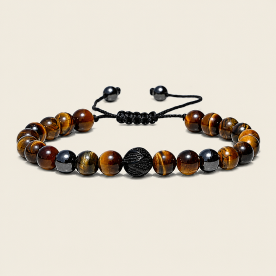 A beaded bracelet made of polished tiger's eye beads in brown and black, with a textured black central bead and a black adjustable cord closure, shown on a light beige background.