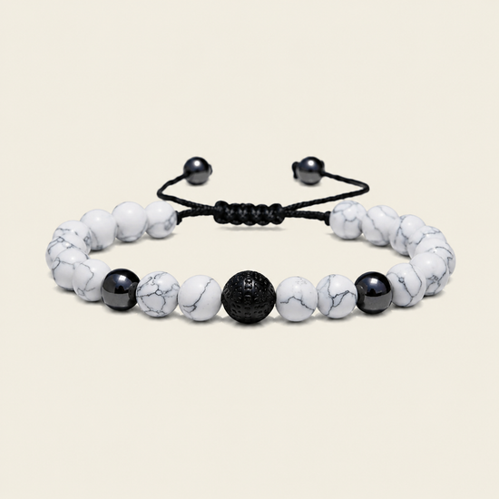 A beaded bracelet with white marble beads, a textured black central bead, and black accent beads on a black adjustable cord, shown on a light beige background.