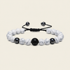 A beaded bracelet with white marble beads, a textured black central bead, and black accent beads on a black adjustable cord, shown on a light beige background.
