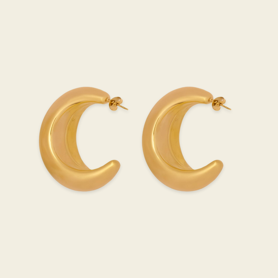 A pair of gold crescent-shaped hoop earrings with a smooth, polished finish, displayed on a light cream background.