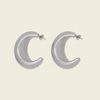 A pair of polished silver crescent-shaped hoop earrings with post backings, displayed on a solid light beige background.