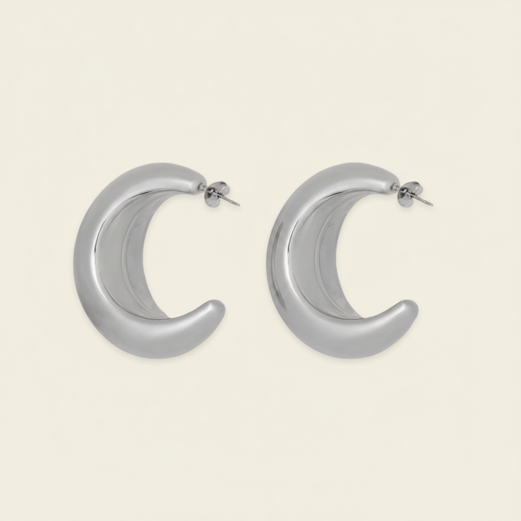 A pair of polished silver crescent-shaped hoop earrings with post backings, displayed on a solid light beige background.