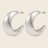 A pair of large, polished silver crescent-shaped hoop earrings on a solid light beige background.