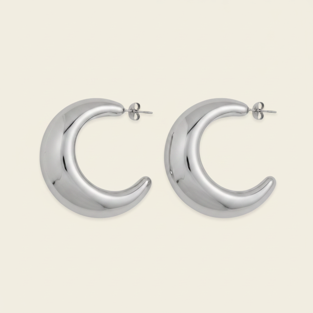 A pair of polished silver crescent-shaped hoop earrings with post backings, displayed on a light cream background.