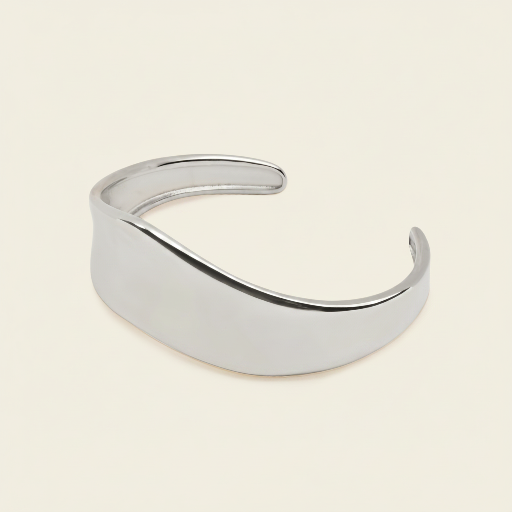 A polished silver-toned metal cuff bracelet with a smooth, curved, open design, displayed on a solid light cream background.