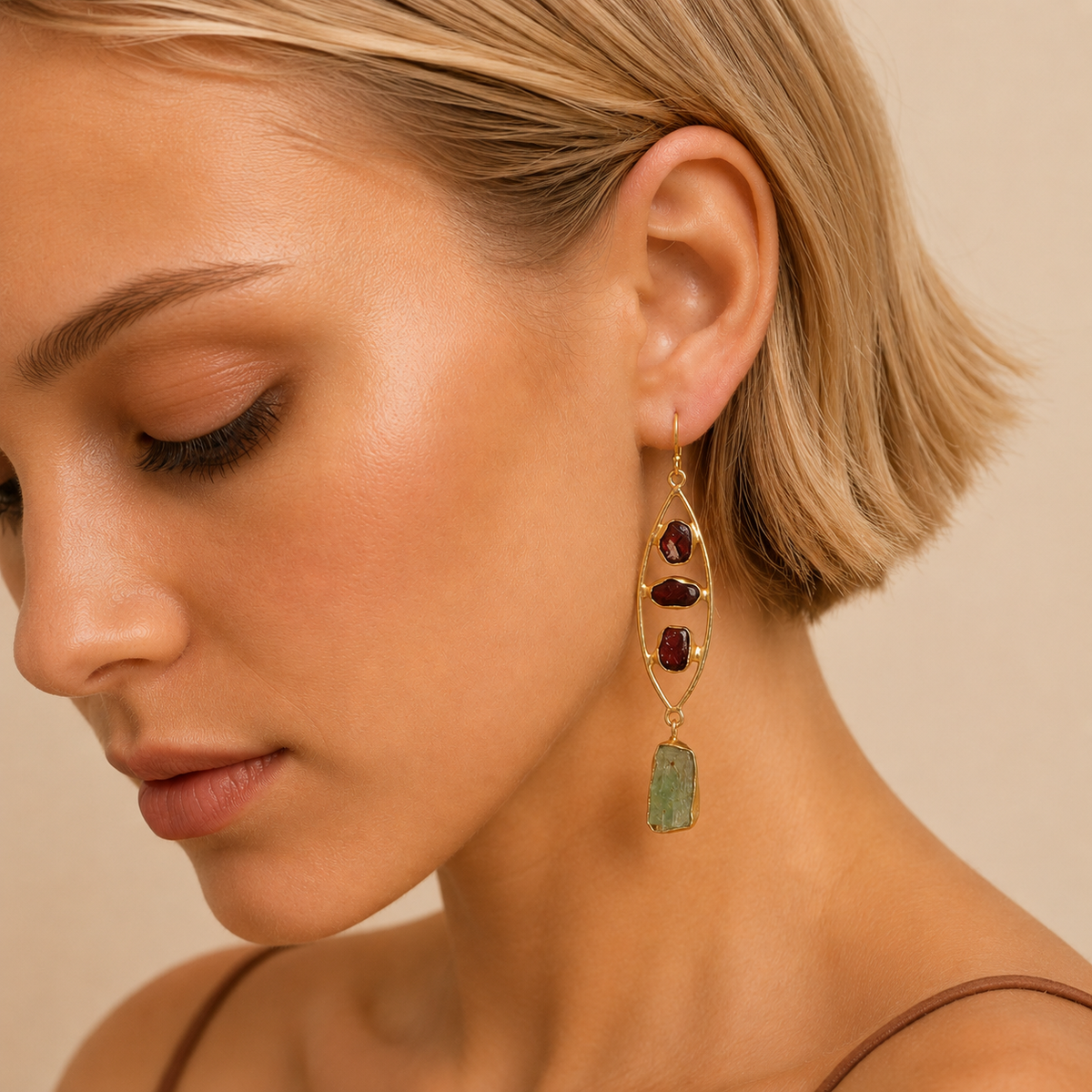 Close-up of a woman wearing gold earrings with red and green stones on a beige background