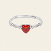 A silver-toned adjustable ring with a heart-shaped red gemstone in the center and small clear accent stones along the band, shown on a light cream background.
