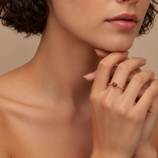 Close-up of a woman's neck and hand wearing a red gemstone ring on a neutral background