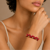 Close-up of a woman's arm wearing a red and gold beaded bracelet against a neutral background