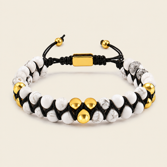 A beaded bracelet featuring white and gray marbled beads, polished gold-tone accent beads, and a black adjustable cord with a gold clasp, shown on a light beige background.