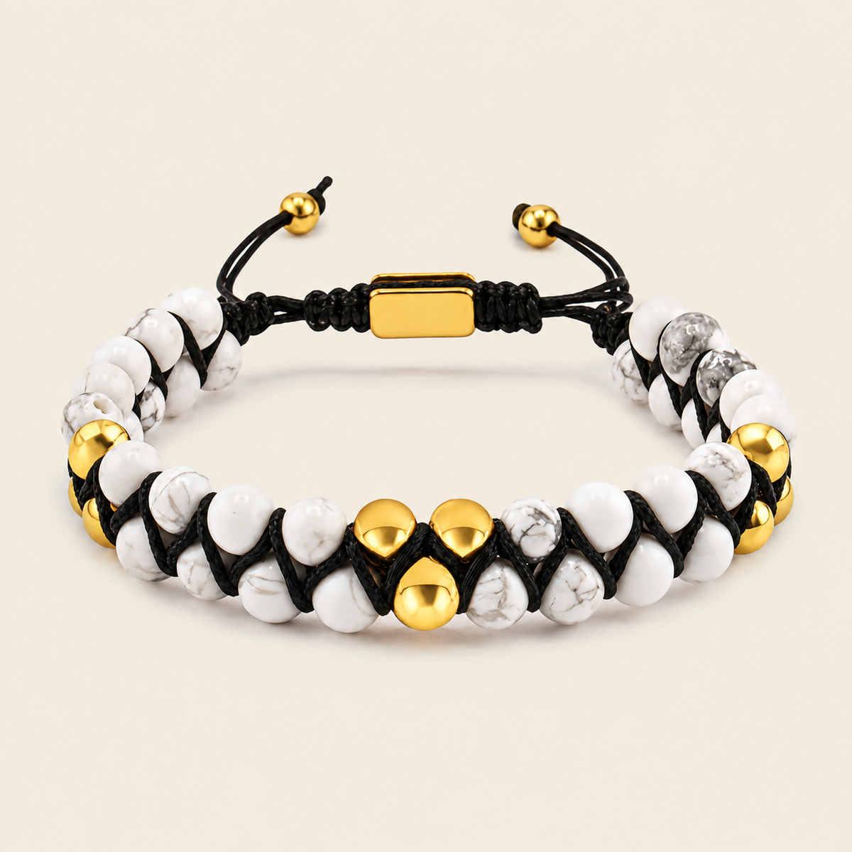 A beaded bracelet featuring white and gray marbled beads, polished gold-tone accent beads, and a black adjustable cord with a gold clasp, shown on a light beige background.