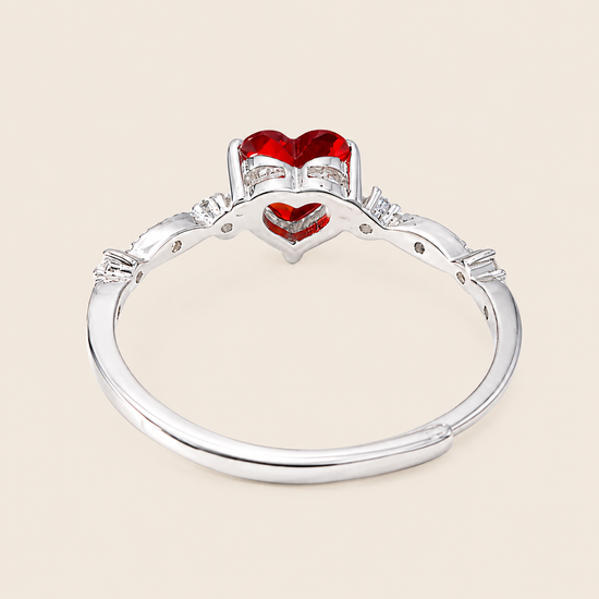 Silver ring with red heart-shaped gemstones on a beige background