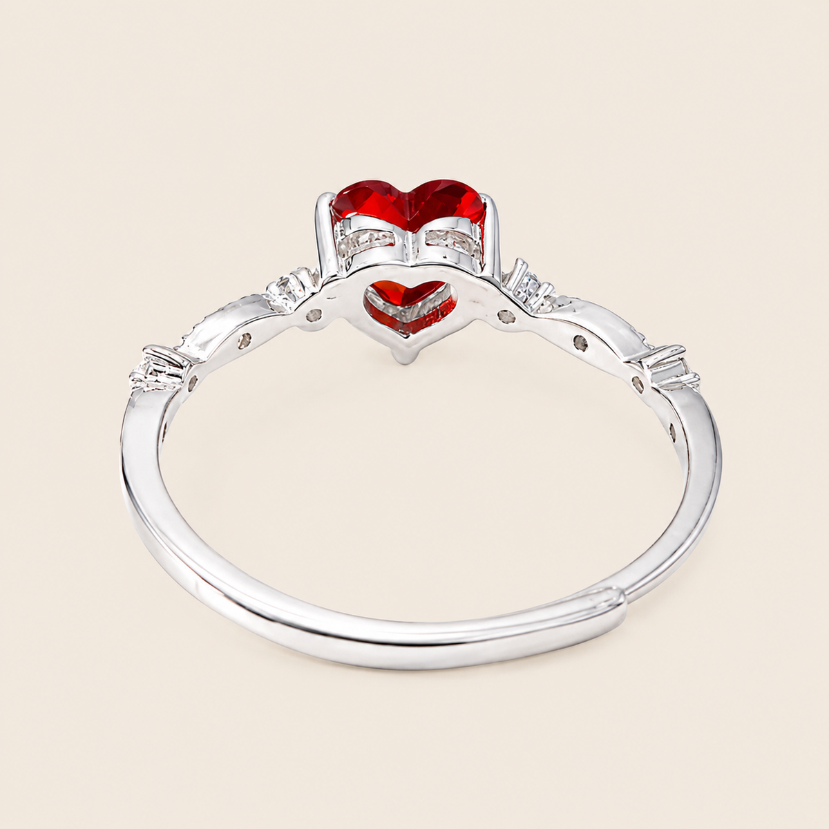 Silver ring with red heart-shaped gemstones on a beige background